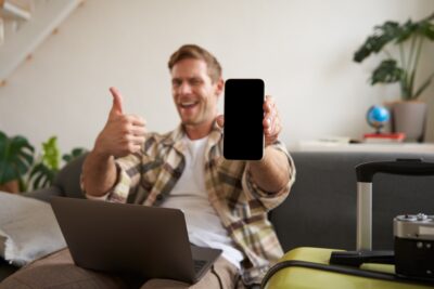Portrait of man, tourist shows his mobile phone screen, recommends travel app, sitting with